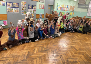 Spotkanie klas I-III na korytarzu. Każde dziecko trzyma w górze swoją ulubioną maskotkę.