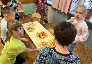 Poczęstunek dla uczniów naszej szkoły. Na stoliku leżą pokrojone na talerzach jabłka i marchewki, uczniowie się częstują.