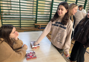 Stanowisko z losowaniem przyszłości. Uczennica klasy VI z zamkniętymi oczami i uśmiechem na twarzy losuje informacje na temat swojej przyszłości