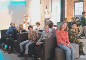 Uczniowie klas II i III w holu Teatru Pinokio siedzą na kanapach oczekują na wejście na przedstawienie ,,Dzieci z Bullerbyn"
