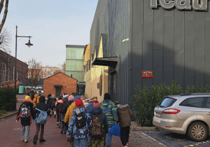 Uczniowie klasy II i III zmierzają do teatru. Po prawej stronie znajduje się budynek z napisem ,,Teatr"