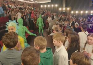 Uczniowie klasy IV po przedstawieniu ustawieni w kolejce przed aktorem z przedstawienia czekają aby przybić ,,Piątki"