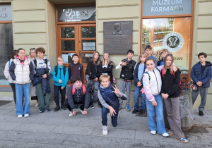Uczniowie klasy VI stoją na tle Muzeum Farmacji na ulicy Piotrkowskiej. Dwóch uczniów kuca reszta stoi.