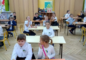 Uczniowie siedzący przy ławkach w klasie