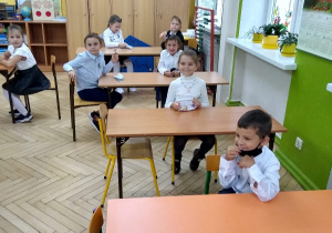 Uczniowie siedzący przy ławkach w klasie