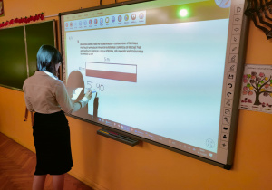 Uczennica klasy VIII rozwiązuje równanie przy tablicy multimedianej związane z flagą Polski