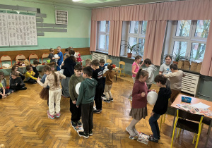 Konkurs Misiowy Taniec-cuczniowie stoją na gazetach a pomiędzy brzuszkami mają balony, tańczą w rytm muzyki.