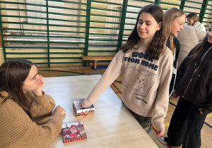 Stanowisko z losowaniem przyszłości. Uczennica klasy VI z zamkniętymi oczami i uśmiechem na twarzy losuje informacje na temat swojej przyszłości