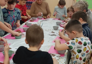 Uczniowie klasy drugiej wraz z nauczycielem z zaangażowaniem wykonują czekoladowe bombki