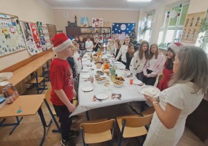 Klasa piąta wraz z wychowawcą siedzi przy stołach podczas swojej wigilii