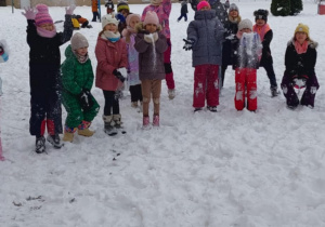 Uczniowie klas I-III podczas zabaw na śniegu przed szkołą. Podrzucają śnieg do góry