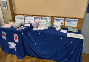 Stół przykryty niebieskim obrusem ozdobiony białymi koralikami, na nim leż przygotowane dla laureatów konkursu nagrody - pięknie zapakowane.