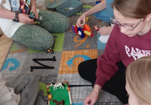 Uczniowie siedzą na dywanie przed nimi leż klocki LEGO i układają z nich stadninę dla koni.