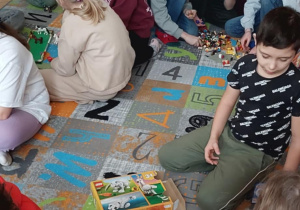 Klasa III siedzi na dywanie w sali, wszyscy zajęci układaniem budowli z klocków LEGO