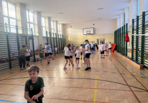 Dzieci na sali gimnastycznej rozgrzewają się przed treningiem JUDO. Ćwiczenia odbywają się w parach. Dzieci ćwiczą z uśmiechem na twarzy i dużym zaangażowaniem