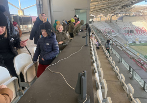 Stadion ŁKS, uczestnicy znajdujący się w najwyższym miejscu na stadionie, czyni na stanowiskach komentatorskich. W tle krzesełka trybun.