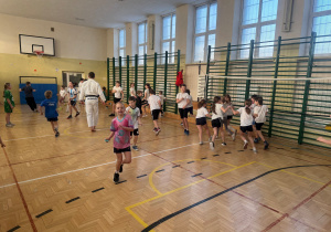 Zajęcia z JUDO na sali gimnastycznej, uczestnicy rozproszeni po sali gimnastycznej bawią się w berka