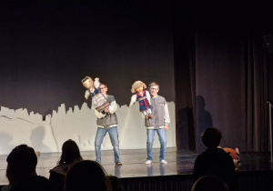 Scena teatru, a na niej dwóch uczestników, którzy tańczą trzymając w rękach lalki do przedstawienia