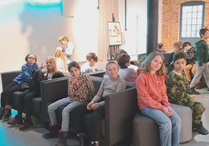Uczniowie klas II i III w holu Teatru Pinokio siedzą na kanapach oczekują na wejście na przedstawienie ,,Dzieci z Bullerbyn"