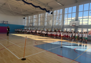 Uczniowie ze szkół podstawowych biorący udział w zawodach, soją ustawieni w jednym długim rzędzie. Przed zawodnikami stoi nauczyciel i wyjaśnia wszystkie zasady i regulaminy obowiązujące podczas zawodów.