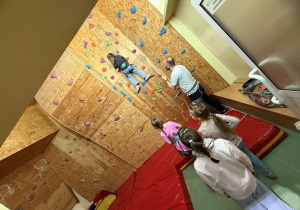 Przyszli uczniowie mogli skorzystać w naszej szkole ze ścianki wspinaczkowej. Chętnie brali udział we wspinaczce. Na zdjęciu dziecko wspina się w górę i jest ustawiona kolejka innych dzieci do wspinania.