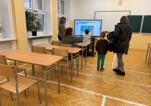 Rodzice i przyszli uczniowie na ekranie dotykowym szukają różnic na przedstawionych obrazkach.