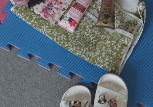 Na podłodze leży zestaw do relaksu- kremy maseczki, ręcznik oraz klapki.