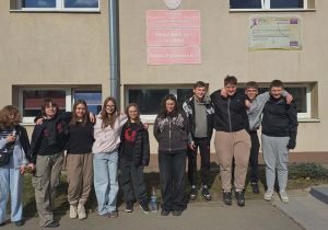 Uczniowie klasy VIII przed wejściem do szkoły pozują do zdjęcia trzymając się za ramiona