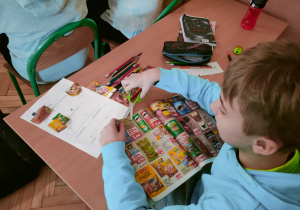 Uczeń precyzyjnie wycina z kolorowej gazetki promocyjnej wybrane produkty, które następnie trafią na jego kartę pracy w ramach matematycznego zadania o zakupach.
