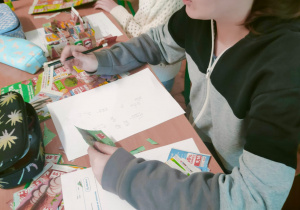 Uczennica klasy 5 w skupieniu analizuje wybrane z gazetki produkty i dokonuje obliczeń na karcie pracy, dbając o to, by domowy budżet został poprawnie rozliczony.