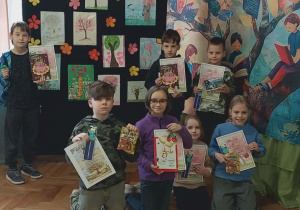 Uczniowie klas I-III pozują do zdjęcia na tle swoich prac i wielkiego baneru przedstawiającego drzewo a na drzewie są dzieci,które czytają książki. Nasi uczniowie na zdjęciu prezentują dyplomy i nagrody konkursowe.
