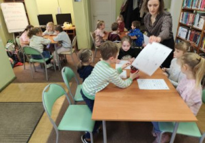 Uczniowie klas I i II w bibliotece rejonowej, otrzymają kartę z zagadkami. Uczniowie siedzą przy stolikach.