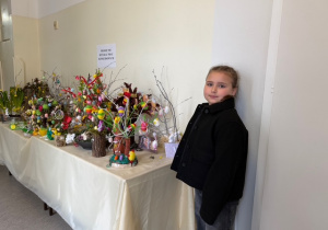 Uczennica klasy III stoi przy stole nakrytym białym obrusem a nam stoją wszystkie prace uczniów