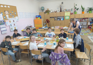 Uczniowie klasy 2 pozują do zdjęcia przy stole wielkanocnym, na którym są różnego rodzaju smakołyki. Dzieci uśmiechnięte, w tle sali szafki i tablica korkowa