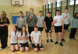 Uczniowie klasy VI na sali gimnastycznej pozują do zdjęcia z przypiętym żonkilami do ubrań