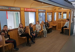 Klasa III w rekonstruowanym pociągu z czasów wojny. Uczniowie siedzą na krzesełkach i pozują do zdjęcia