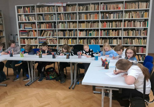 Uczniowie w bibliotece muzeum, siedzą przy stołach i pracują nad wykonaniem zadania z karty pracy.