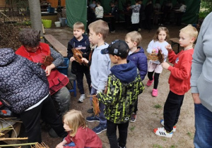 Uczniowie uczestniczą w warsztatach wyplatania wikliny. uważnie przyglądają się co robi pan prowadzący i próbują sami wyplatać koszyki.