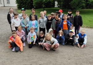 Uczniowie klasy I i II przed dworkiem w Bolimowie pozują do zdjęcia. Dzieci patrzą z uśmiechem na twarzy na osobę robiącą zdjęcie