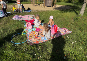 Uczennice rozłożyły koc na trawie i rozmawiając ze sobą zjadają swoje pyszne śniadanie