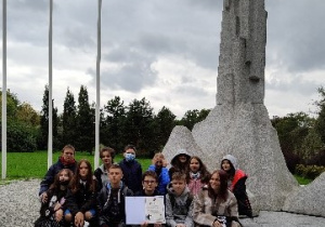 Grupa uczniów prezentuje dyplom pod pomnikiem